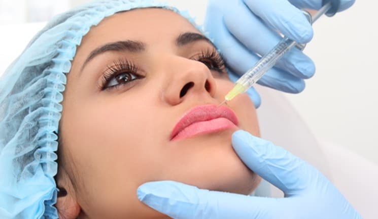 A woman undergoing lip filler safety as a doctor injects the upper lip of a patient.