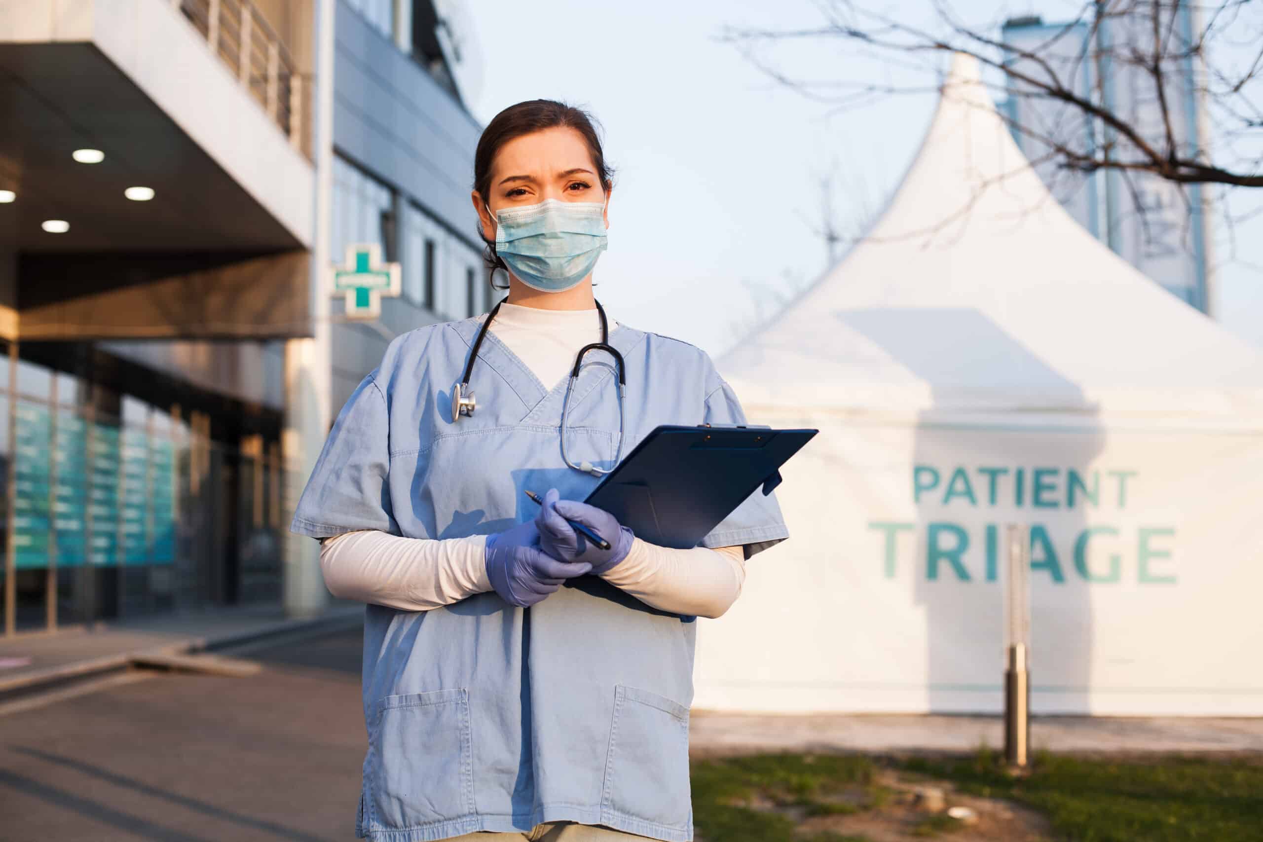 A female medical professional standing infront of a hospital