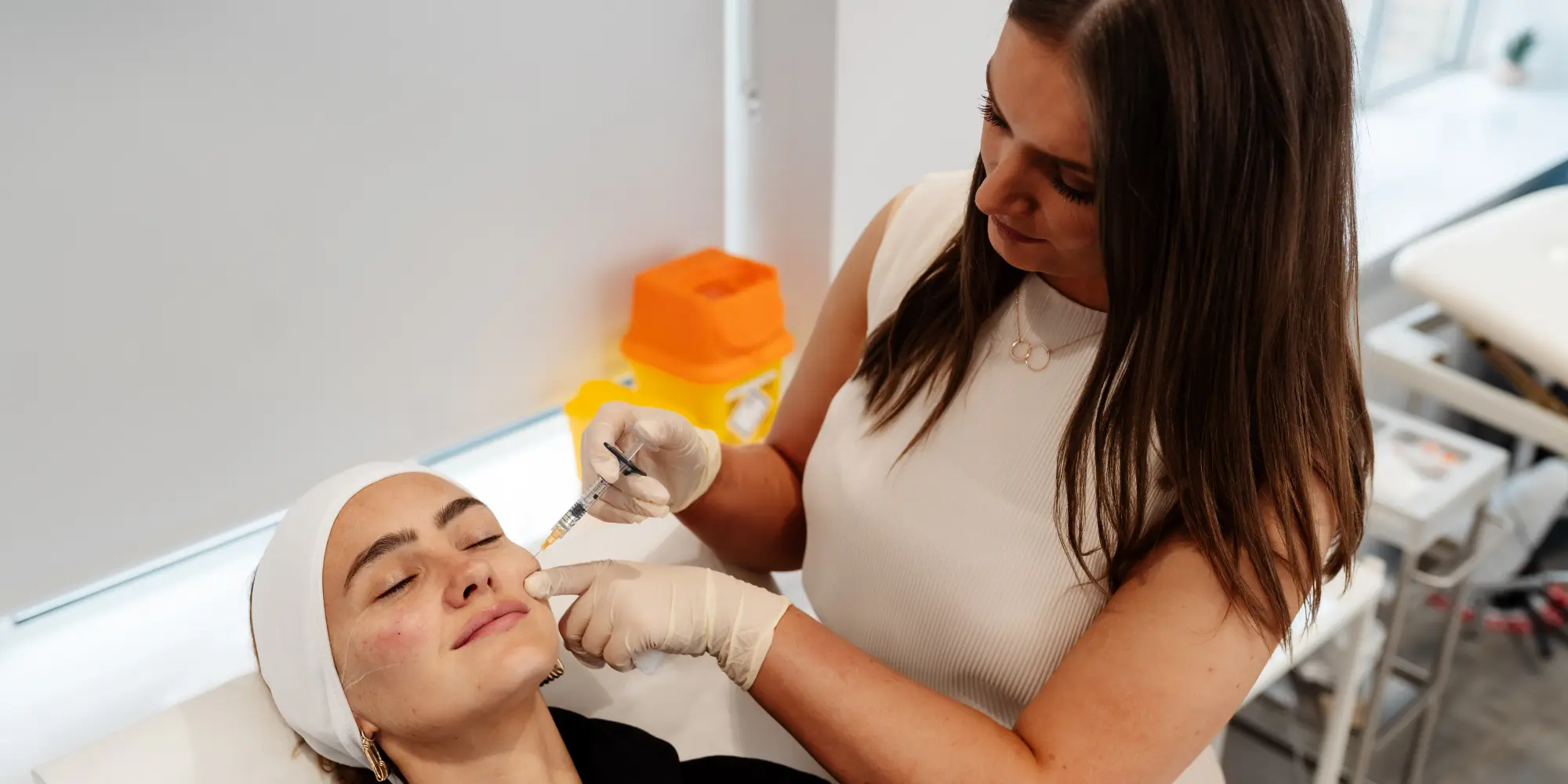 brunette aesthetic practitioner training who is injecting botox to a patient